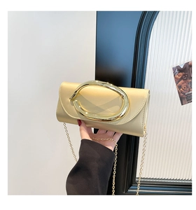 Close-up of champagne gold clutch featuring a decorative metal oval handle and chain strap