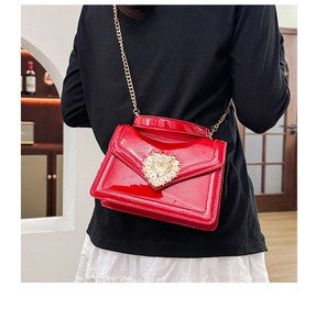 Macro detail of red patent leather shoulder bag featuring a golden heart buckle clasp