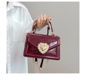 Detail of burgundy patent leather bag with a gold heart buckle and pearl embellishments
