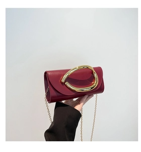 Close-up of deep red leather handbag with oversized curved gold metal handle and chain