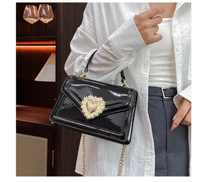 Detail of vintage black patent leather bag with ornate gold heart buckle and chain strap