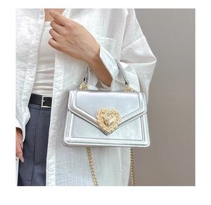 Detail of silver crossbody bag featuring a golden heart-shaped baroque buckle with crystals