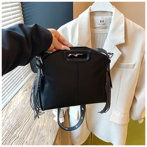 Détail du sac à main en cuir noir avec franges et poignée ajourée sur fond de costume blanc