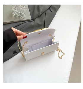 Detail of white glossy PU leather envelope bag with gold magnetic clasp and chain