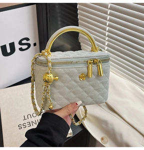 Detail of grey quilted handbag featuring gold metal handle and dual zipper design