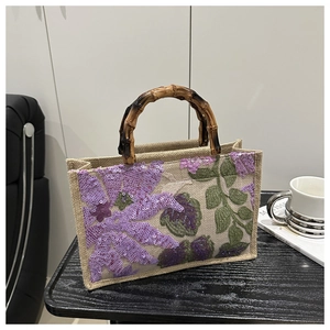 Close-up of ethnic straw tote bag featuring floral sequin embroidery and bamboo handles