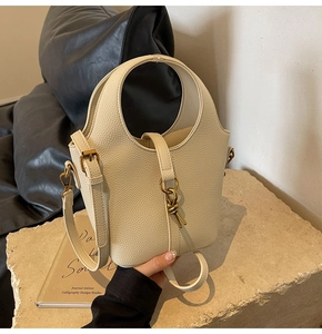 Détail du sac seau beige texture lychee avec boucle nœud doré sur surface en pierre