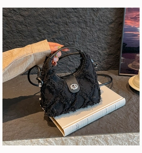 Dettaglio della borsa a mano nera in denim con frange, chiusura a scatto e tracolla