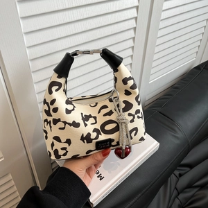 Cow print half-moon handbag with black handle and heart charm on a white background