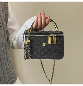 Detail of black woven denim quilted bag featuring a golden camellia logo and metal handle