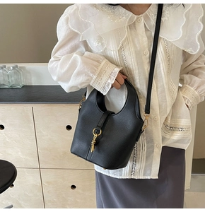 Détail du sac seau en cuir noir avec boucle H dorée et bandoulière nouée élégante