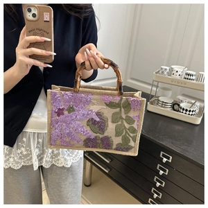Detail of jute handbag featuring purple floral embroidery and vintage bamboo handle