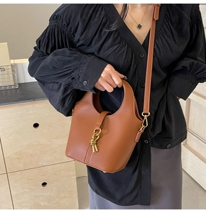Détail d'un sac seau en cuir marron à motif litchi avec breloque noeud doré et bandoulière