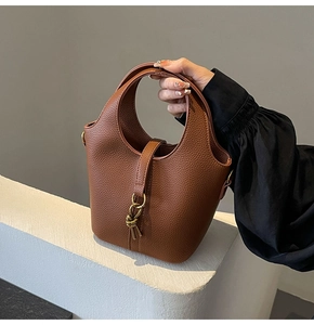 Détail du sac seau en cuir litchi caramel avec anneau métallique doré et nœud en cuir