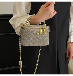 Detail of quilted beige square bag featuring gold flower accent and chain strap