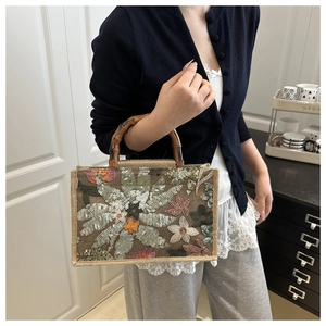 Close-up of sequin floral embroidery and bamboo handle on woven linen handbag
