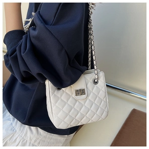 Close-up of white quilted chain bag featuring a metallic turn-lock and leather woven strap