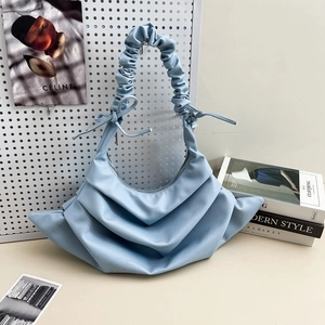 Minimalist light blue pleated crossbody bag displayed on a white pegboard for travel