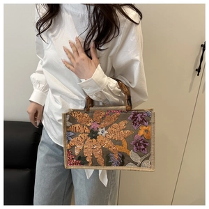 Detail of floral embroidery and sequins on a woven tote bag with bamboo handle