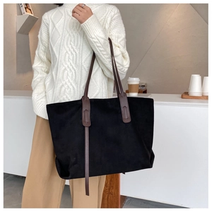 Détail du sac fourre-tout en daim noir avec anses en cuir marron porté par un mannequin