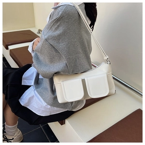 White minimalist shoulder bag with dual front pockets shown worn by a model in a casual setting
