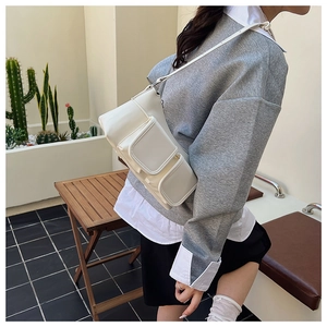White faux leather multi-pocket shoulder bag detail on a neutral outdoor setting