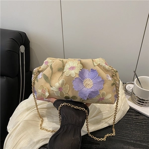Sac nuage brodé de fleurs avec chaîne dorée tenu sur un fond élégant et raffiné
