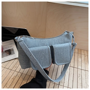 Detail of light blue denim shoulder bag with flap pockets and adjustable strap