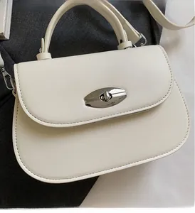 Detail of silver oval metal twist lock and stitching on white semi-circular saddle bag