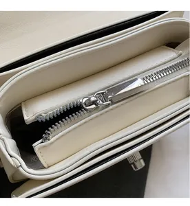 Detail of silver smooth zipper and multi-compartment interior of a cream saddle bag