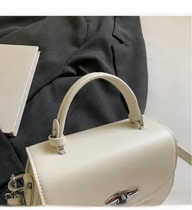 Detail of cream saddle bag with silver hardware and structured handle on a blazer