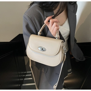 Detail shot of beige saddle bag with silver clasp and slim shoulder strap on stairs