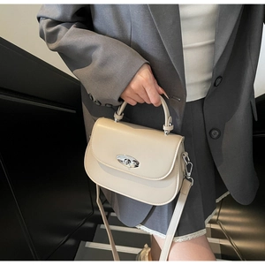 Close-up of minimalist cream saddle bag with silver oval twist lock on grey blazer