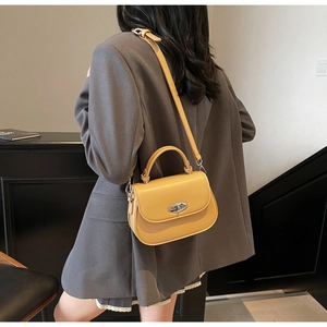Detail of yellow leather saddle bag with silver oval metal lock worn by a model in a suit