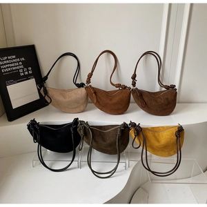 Detail view of crescent crossbody bags in six earthy colors on minimalist white stands