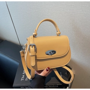 Detail of yellow leather saddle bag with silver oval twist lock on a black book