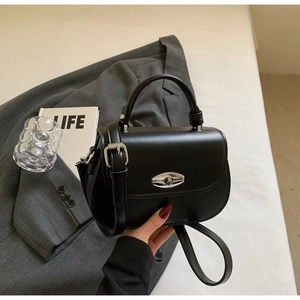 Detail of black saddle bag featuring silver oval metal clasp and smooth PU leather texture