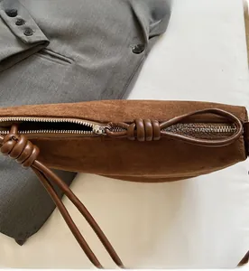 Detail of suede crossbody bag with metal zipper and knotted brown leather handle