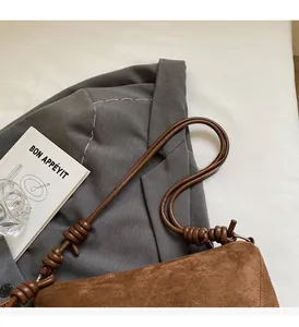 Close-up of brown suede shoulder bag with a knotted strap on a gray blazer