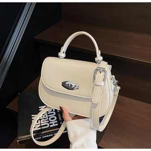 Detail view of cream saddle bag with silver oval twist lock on a wooden step background