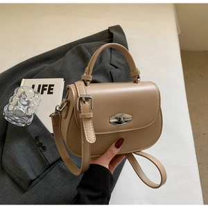 Detailed shot of khaki saddle bag with metal twist lock on a stylish grey blazer background