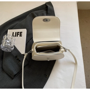 Detail view of cream saddle bag with silver twist lock and interior storage compartments