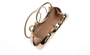 Detail of gold metal clutch with wave texture, round handle, and delicate chain strap