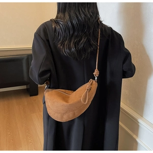 Detail of a brown suede crescent bag with a knot handle detail worn over a black blazer