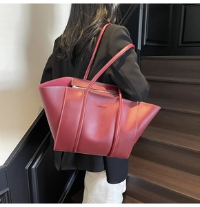Detail view of burgundy leather tote bag with white stitching and metal top zipper closure