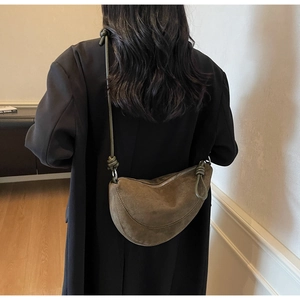 Detail of minimalist dark brown suede crescent bag showing knot strap and crossbody fit