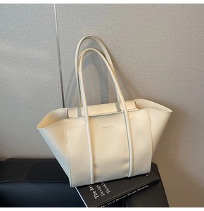 Detail of minimalist cream tote bag showing gold FASHION lettering and smooth leather finish