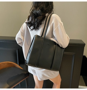 Detail of black faux leather tote bag featuring white contrast stitching and fashion stamp