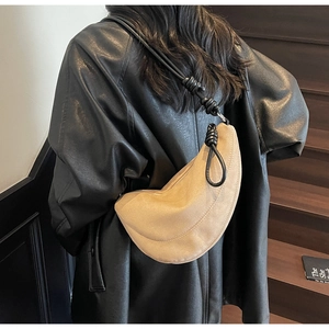 Detail of light brown crescent bag with a decorative black knotted shoulder strap on model