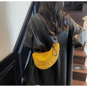 Detail of yellow crescent suede bag with brown braided strap worn on black leather jacket